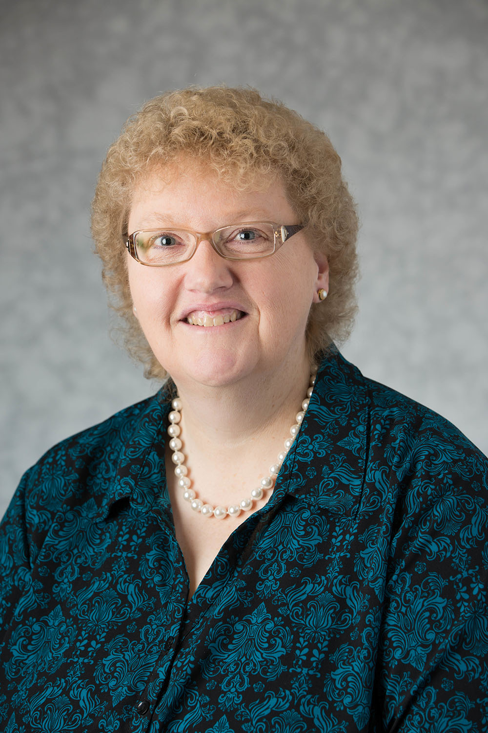 Bonni Kinne in a patterned blue-green shirt with a pearl necklace