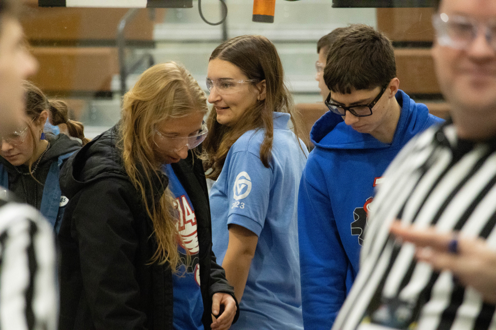 Madelyn Rynsburger in blue golf shirt wears safety goggles at a FIRST Robotics event