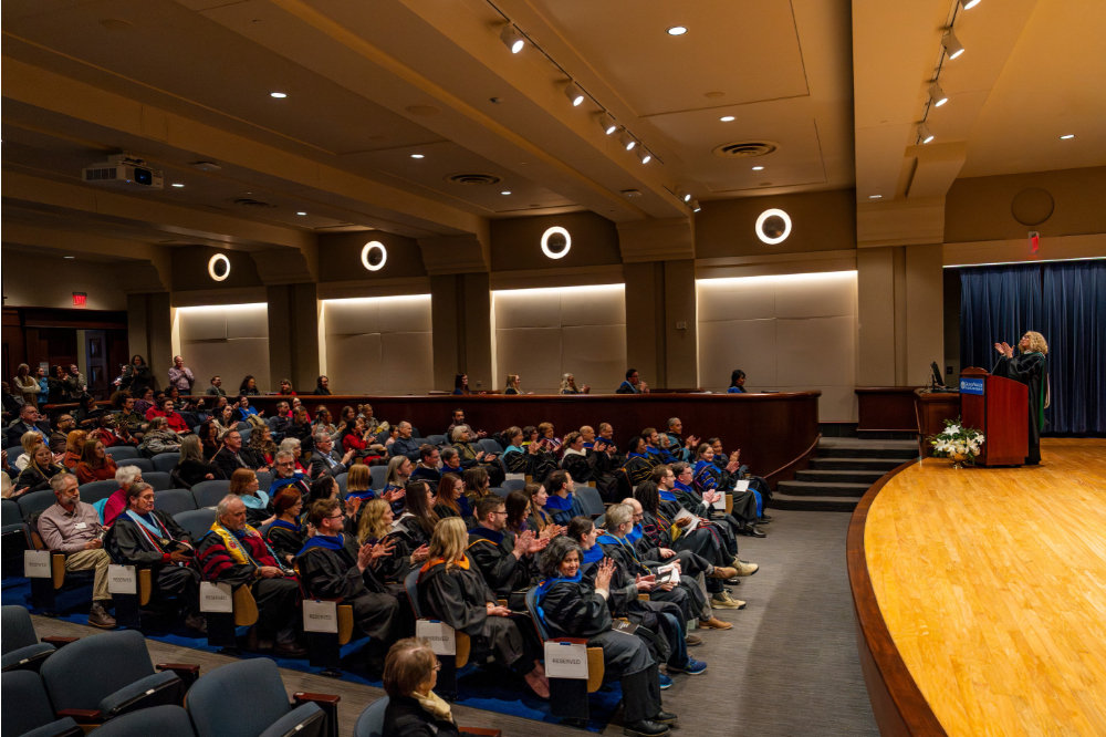 Jennifer Drake on stage in Loosemore Auditorium, audience of faculty members