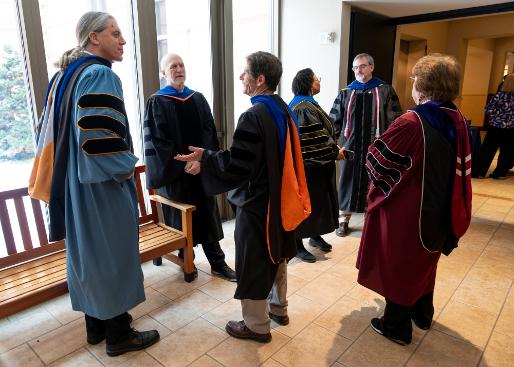 six people in academic regalia stand to chat with each other