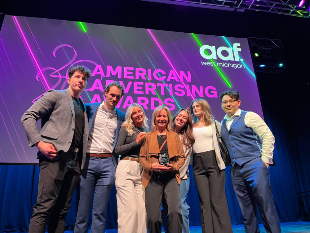 seven people on stage, person in center holding a glass trophy, at the American Advertising Awards