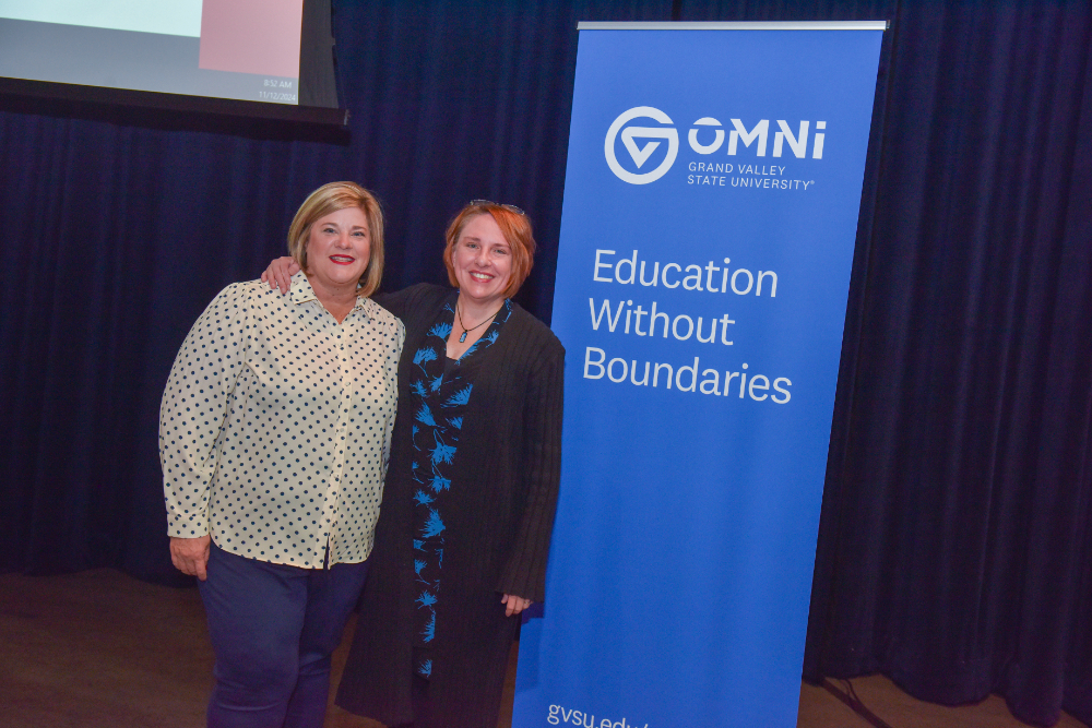 two people standing next to vertical banner for Omni from GVSU, Education Without Boundaries