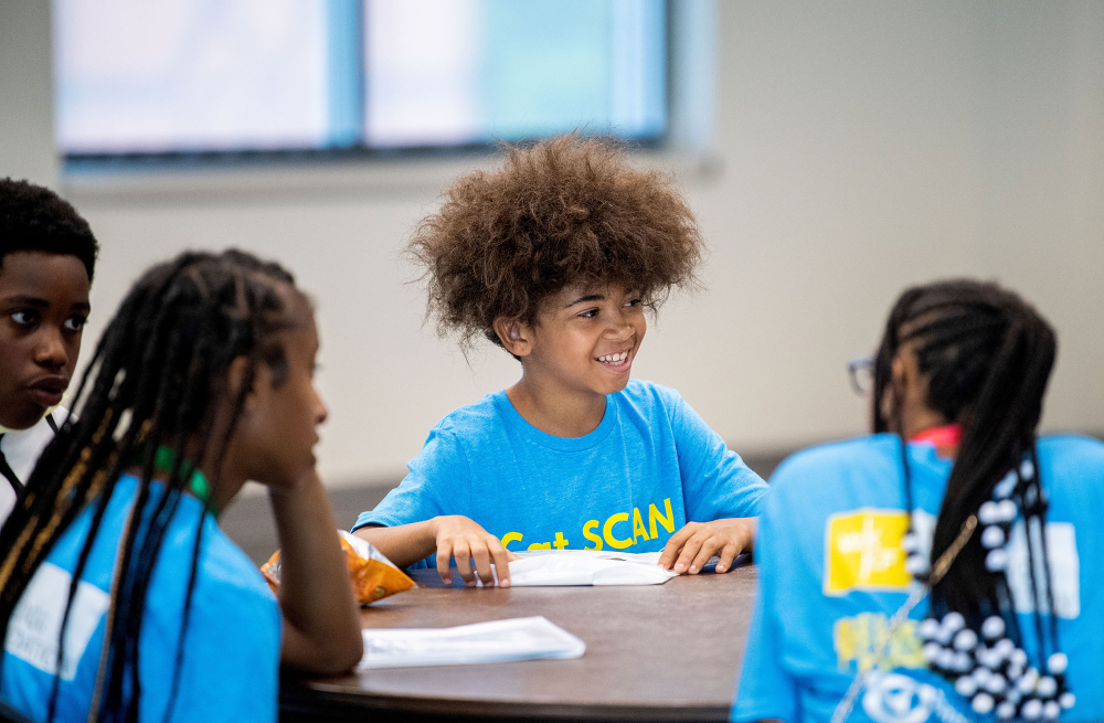 four young middle school students sit at a table all are in blue t-shirts