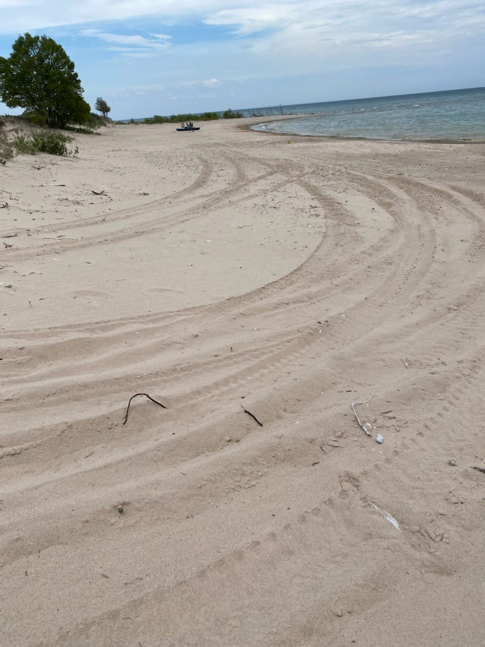 tire tracks on sand near shoreline of lake