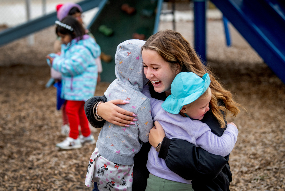two small kids hugging a female student on a playground