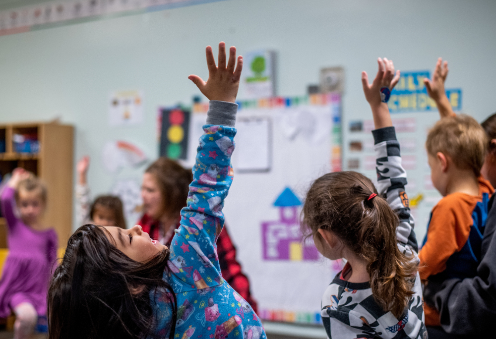 young kids in child care raising their hands