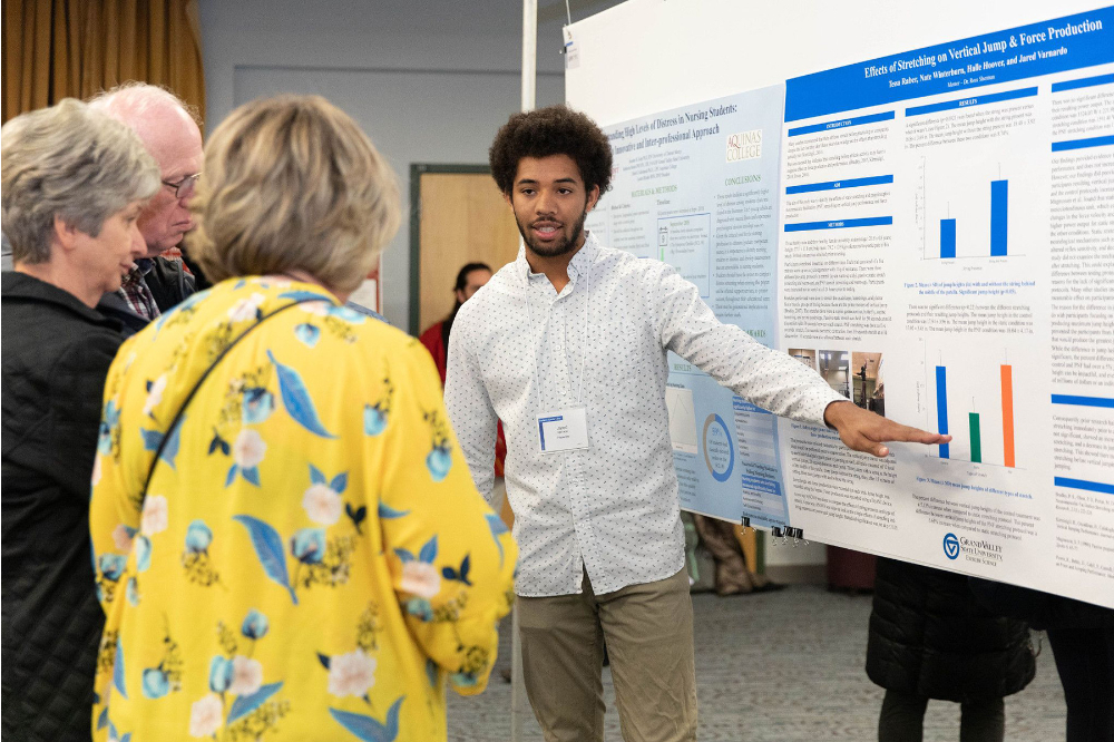 a student points to a poster board as three people look on