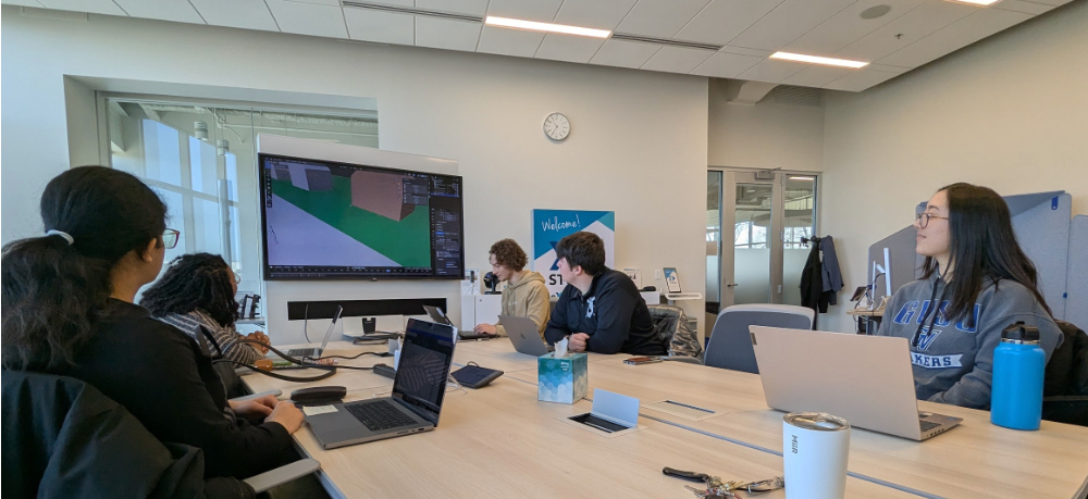 group of students seated at conference table looking at large screen in center front of room