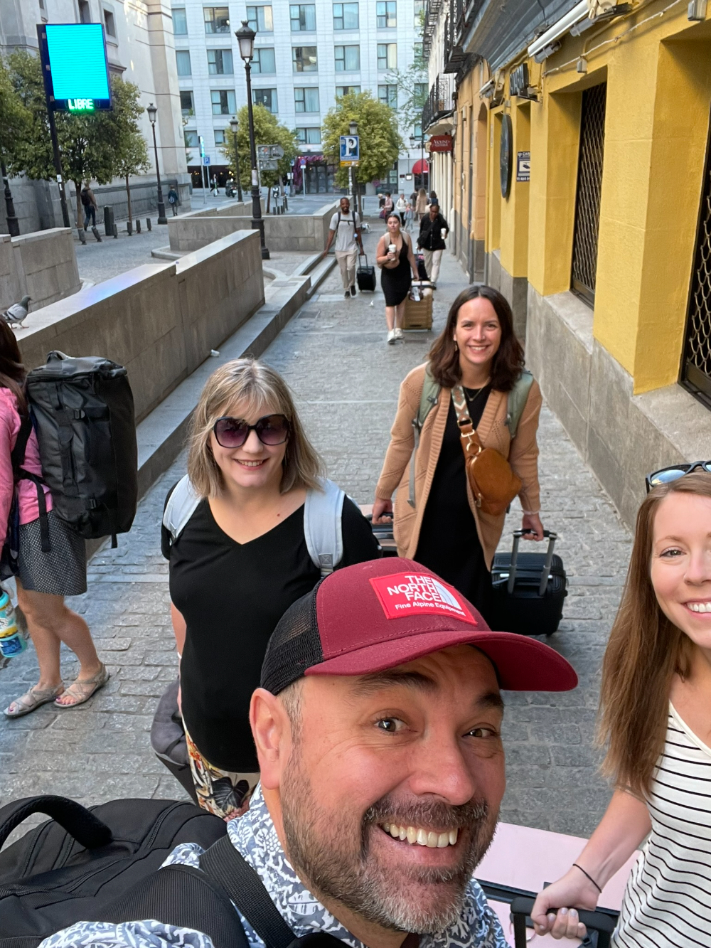 selfie on street in Spain with people behind pulling suitcases