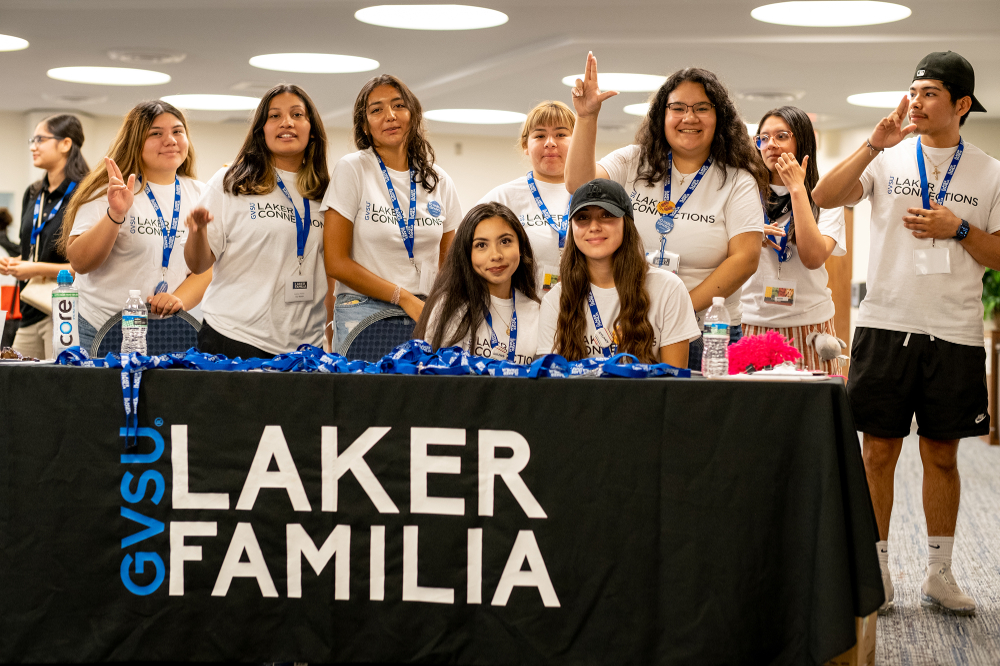 group of students in white tshirts in front of table with Laker Familia draping