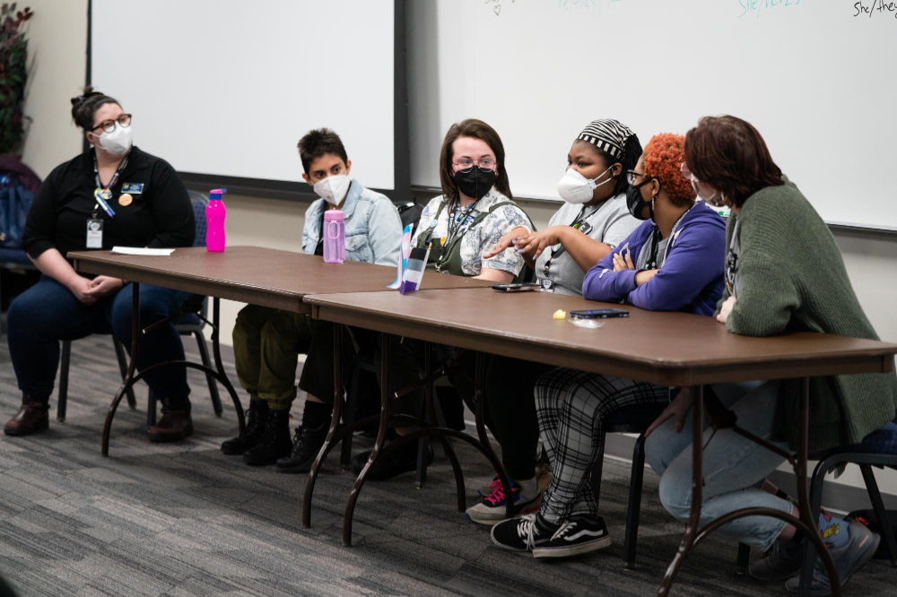five people seated at a table, one person serving as moderator of this panel, whiteboard behind them