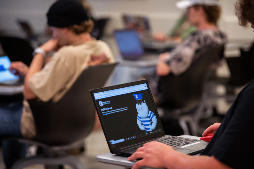 class of students at desks with laptops open, laptop in foreground shows Louie the Laker, it's a Blackboard webpage