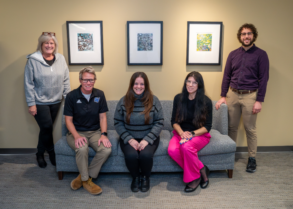 five people, two standing on either end of a couch and three people seated on couch
