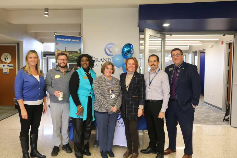 seven people in row standing in hallway in front of GVSU banner and balloons during an open house
