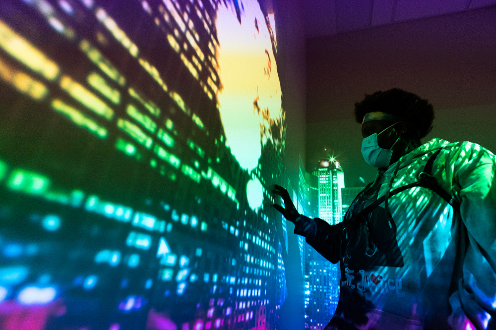 a student in a face mask touches an interactive wall to create the effect of fireworks