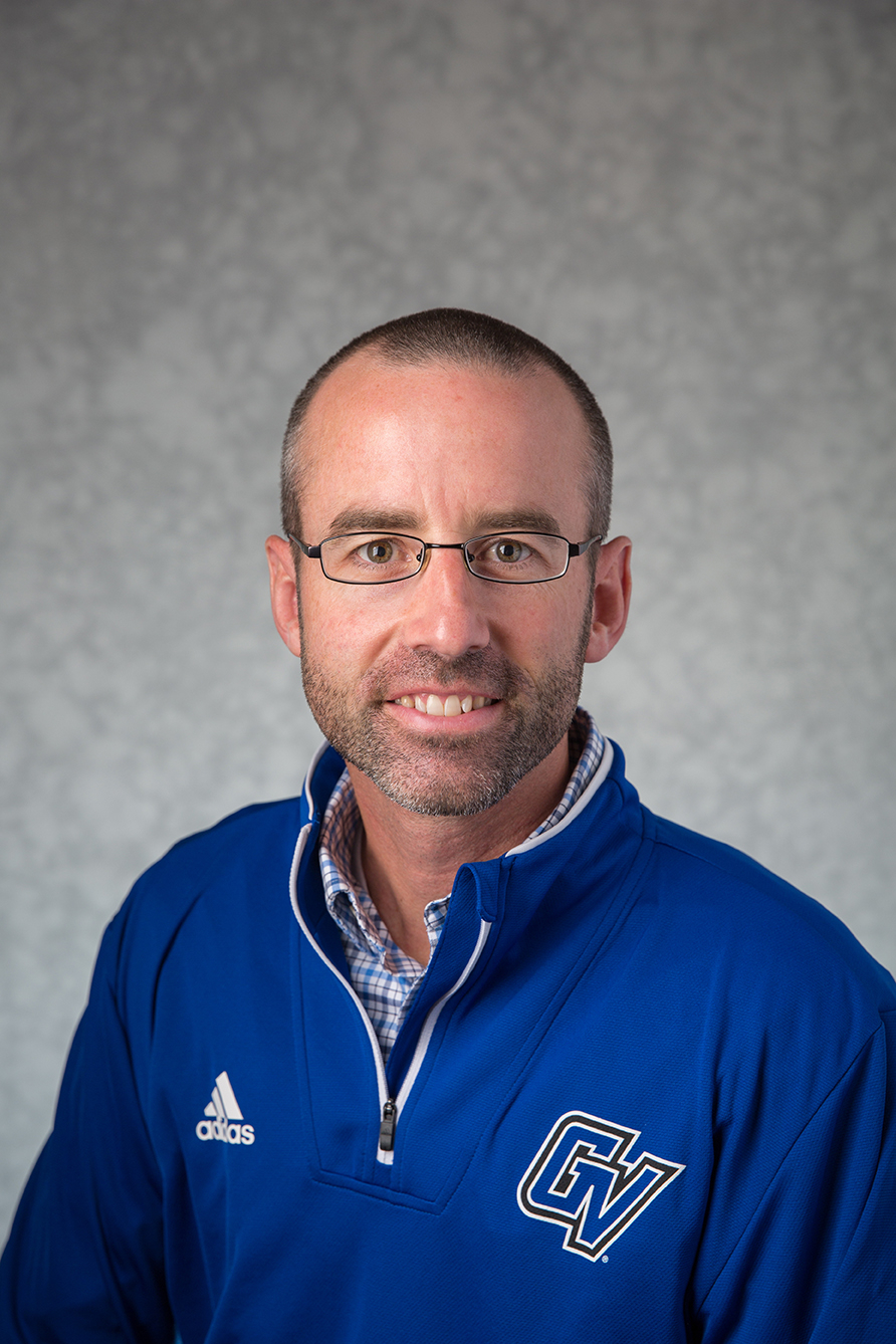 headshot of Jon Coles, who is dressed in GV quarter-zip shirt with button down underneath it. He is wearing glasses