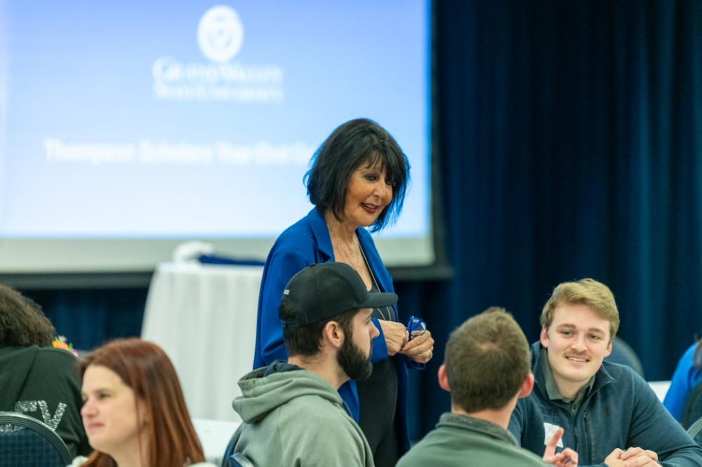 President Mantella talks with students seated at a table while she stands in a blue jacket