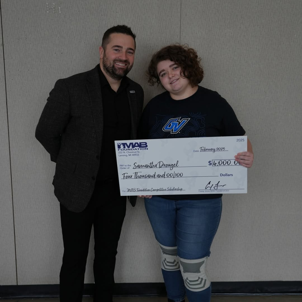 two people, woman on right holding big check from the Michigan Association of Broadcasters