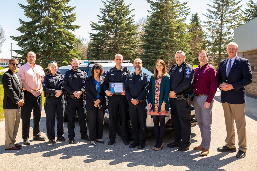 group of people standing, some police officers; officer in middle holding a framed certificate. President Mantella stands in center. They are outside the Facility Services building.