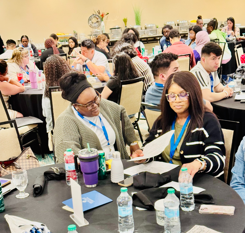 people seated at round tables with paperwork, bottles of water on tables