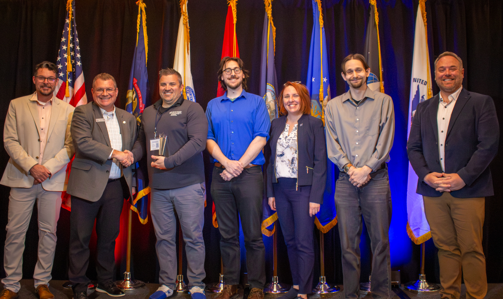 seven people standing in front of row of flags on stage
