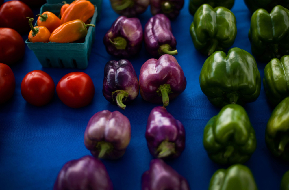 rows of colorful peppers and a few tomatoes from a farm stand table