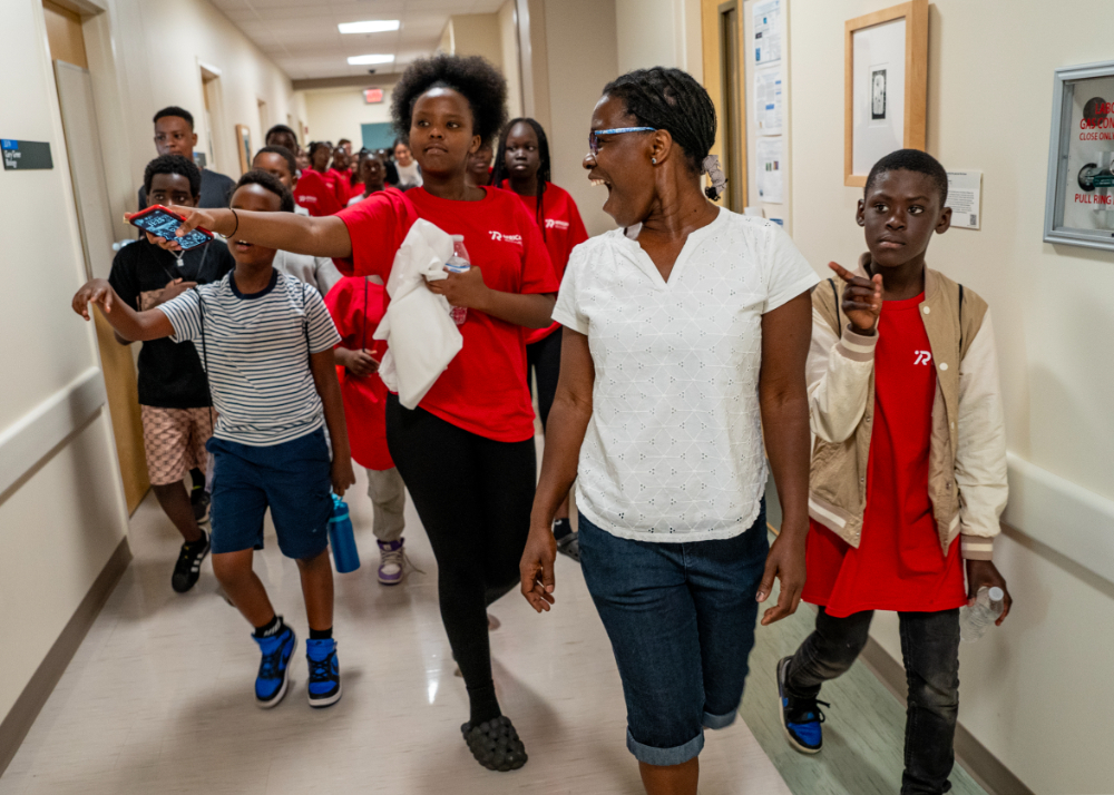 faculty member in white shirt and shorts leads a group of young students in red t-shirts on a tour of Kindschi Hall