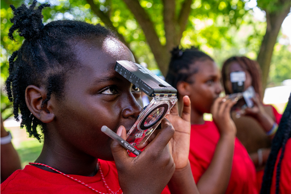 young student in red t-shirt uses a compass outside