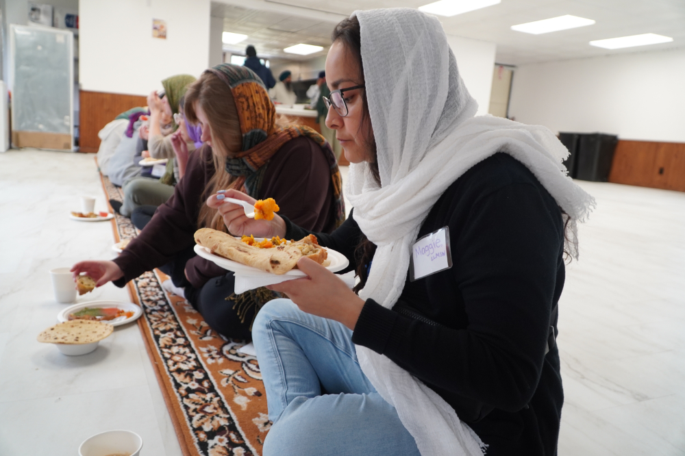 students in head scarves eat a meal while sitting on the floor of a mosque