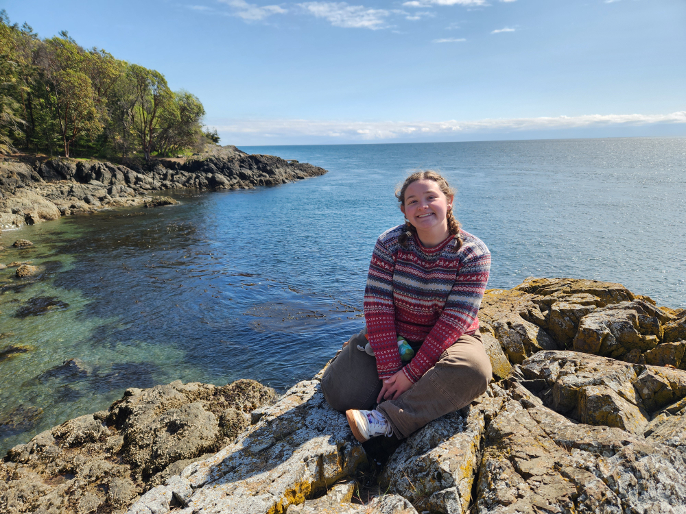 Emmy Scott sitting on rocks near a shoreline