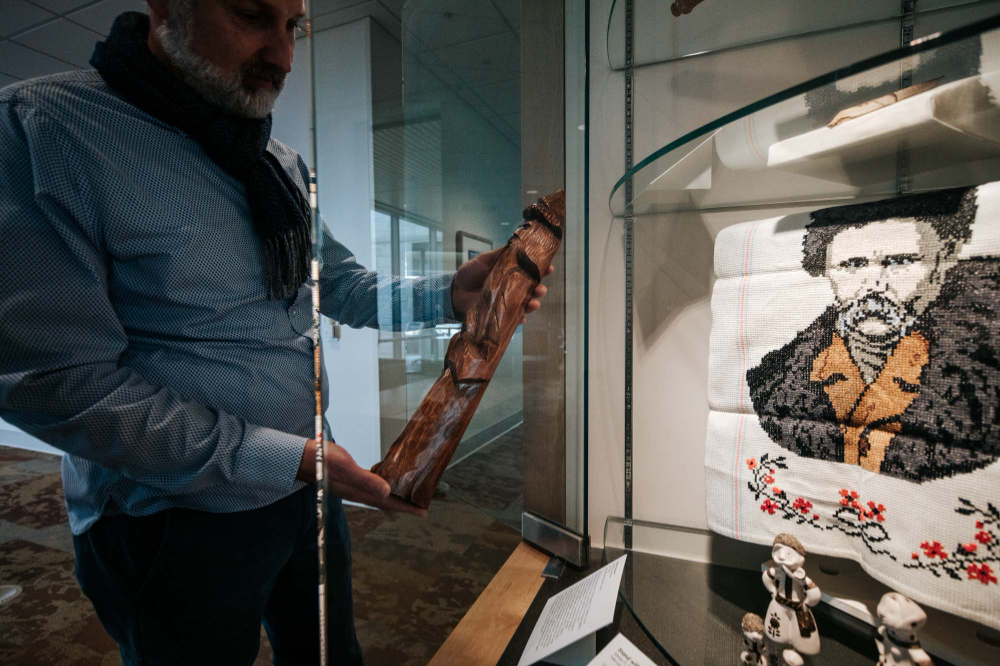 man wearing scarf places a wooden piece of artwork in a display case