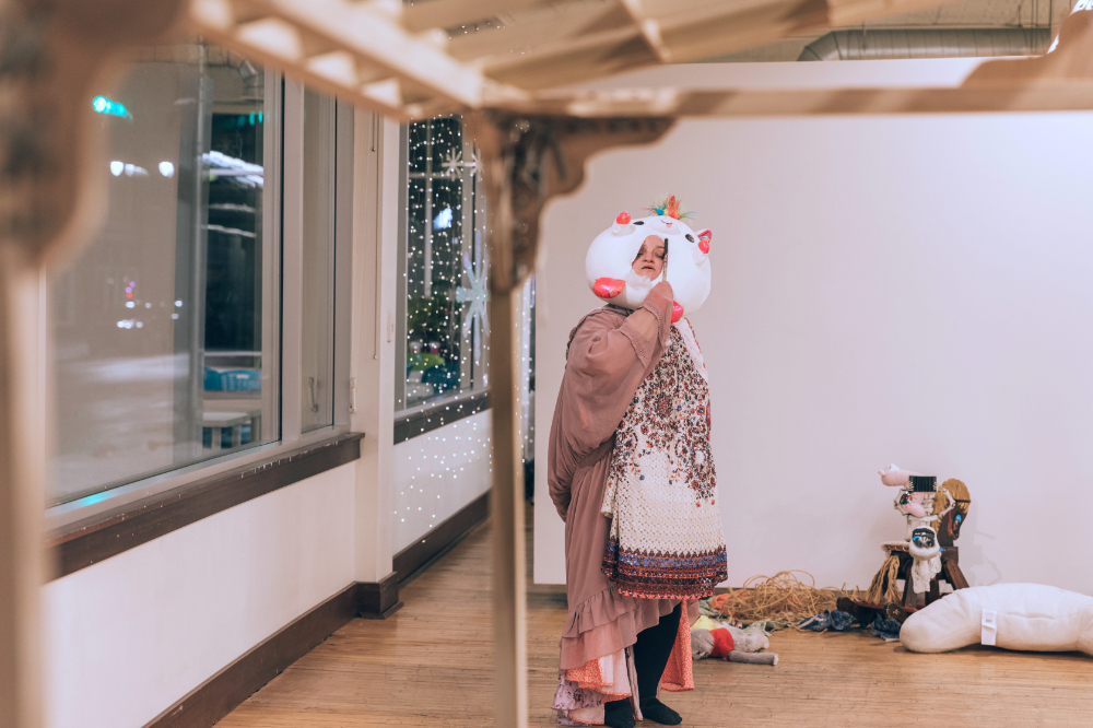 art gallery performance, artist with what looks like paper mache head standing near window