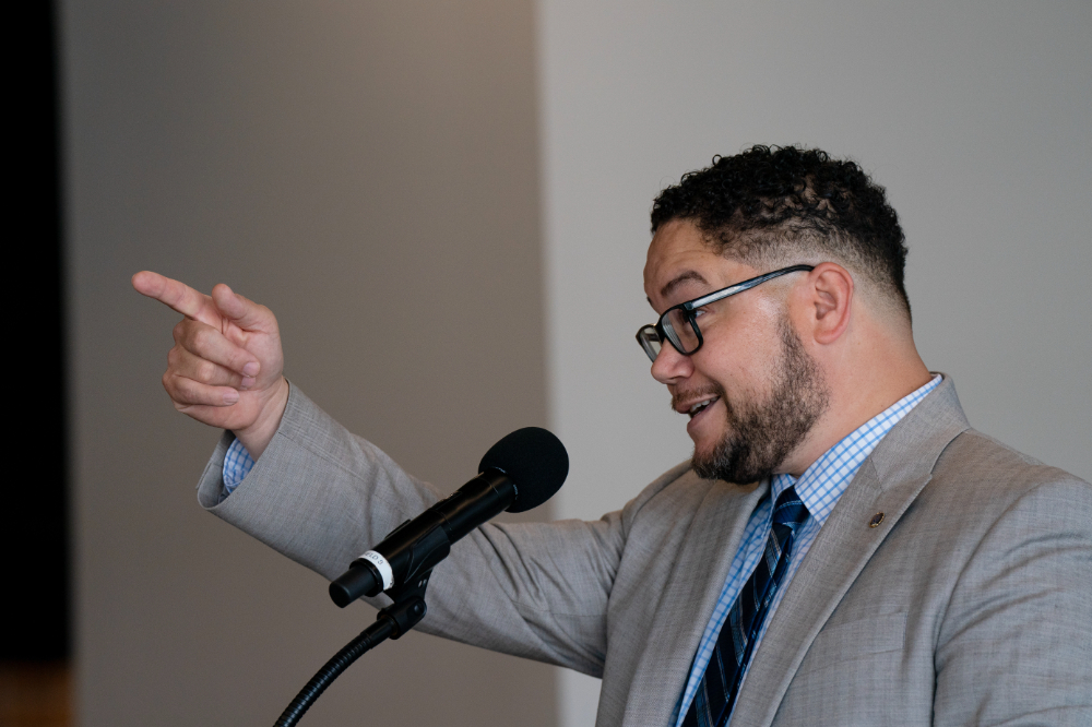 Danny Velez points to the audience while standing at a podium with a microphone