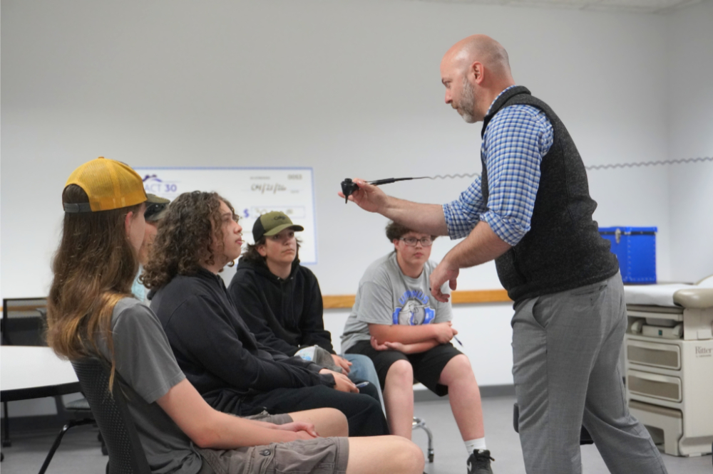 Pat Smith, standing at right, shows an otoscope to four high school students seated in chairs