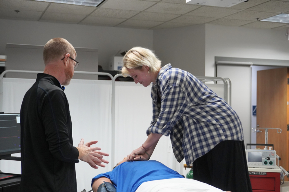 Andy Booth, left, watches as a student leans over a mannequin to press on the chest during CPR training