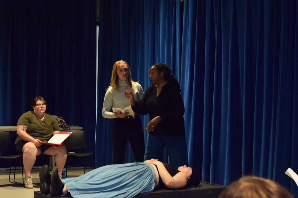 actors and director on stage, one person lying on a table