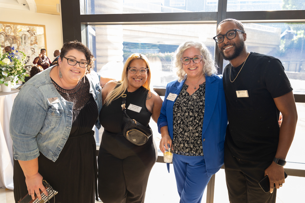 four people gathered for photo, smiling in front of window