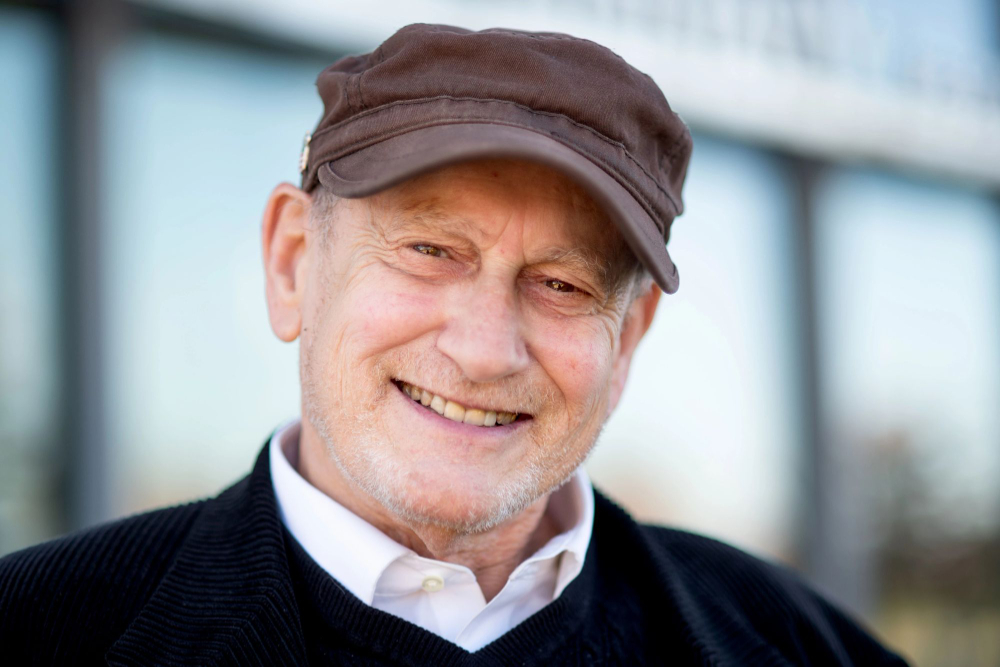 close-up portrait of Roger Ellis with hat on taken outside a glass front building