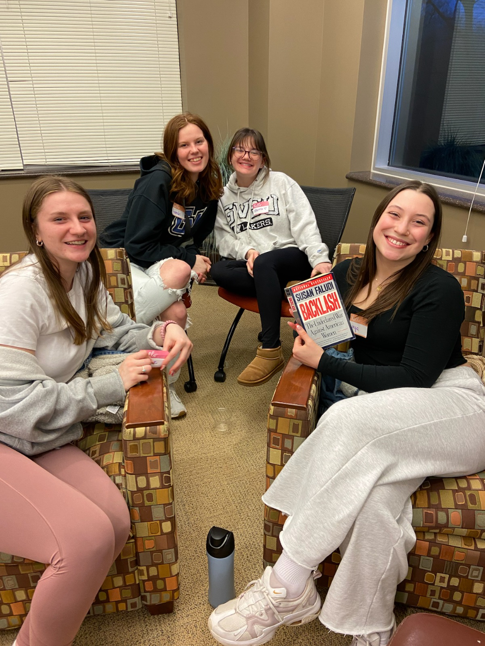 four students in chairs, one holding book in lower right