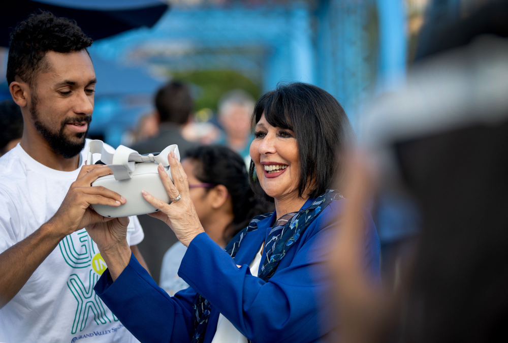 a person hands President Mantella a VR headset to wear on the blue bridge in Grand Rapids during the GR in XR event