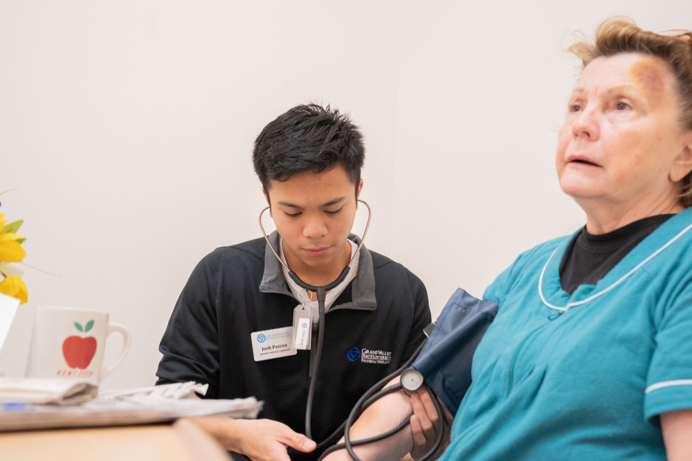 student with stethoscope and blood pressure cuff takes the reading of an elderly woman both are seated