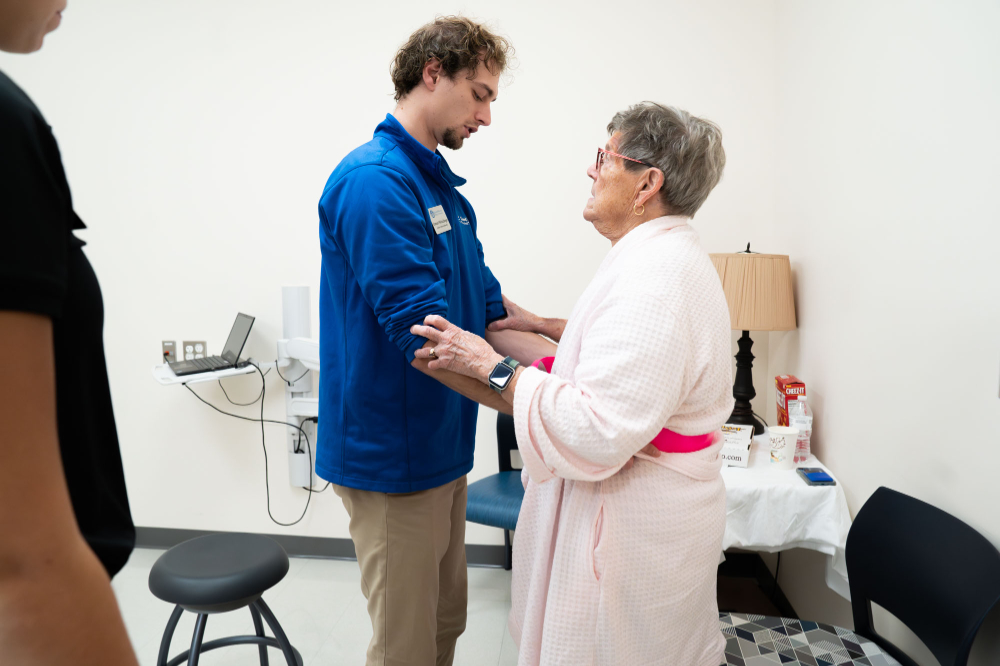 Student assists elderly women in robe to stand by using a belt