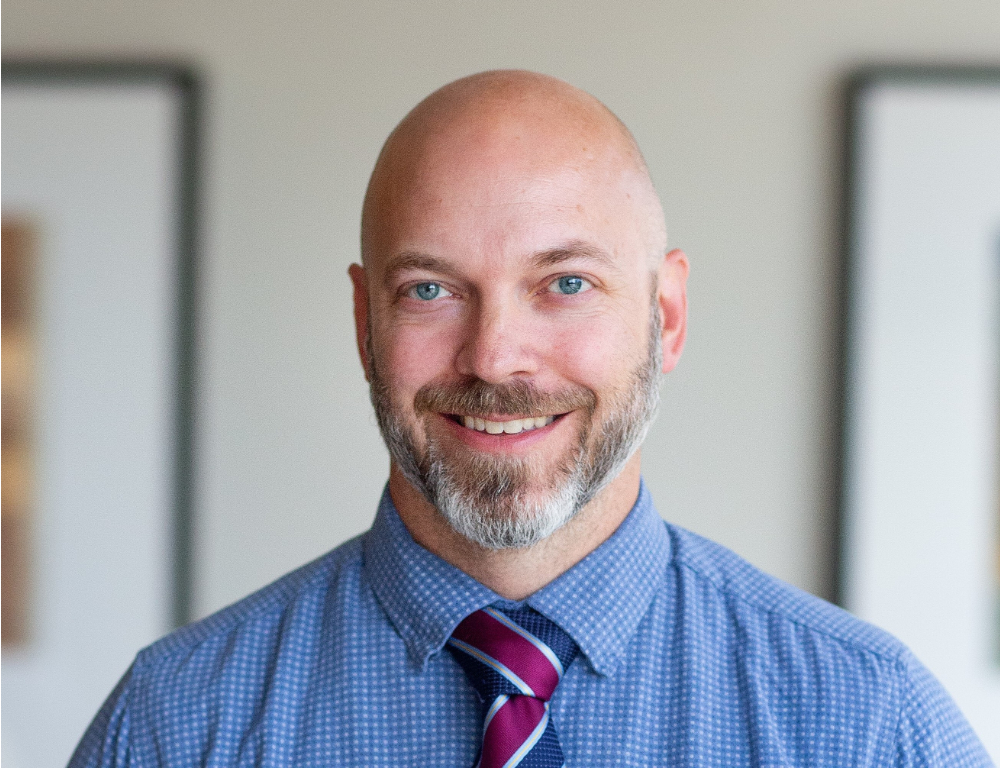 A headshot of a bald man with a beard smiling at the camera.