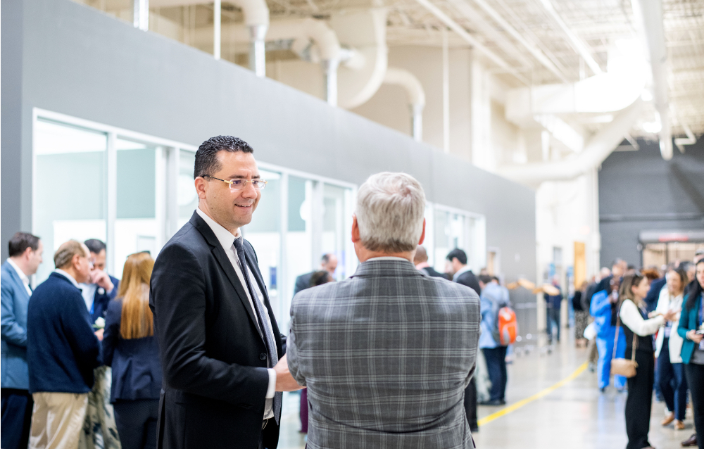 two people in talking with crowds of people gathered on left and right sides of the hallway in background