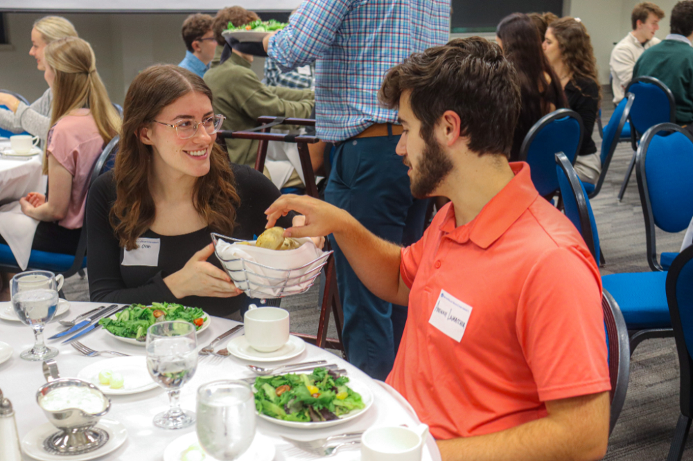 one student passes dinner rolls to her left to another student