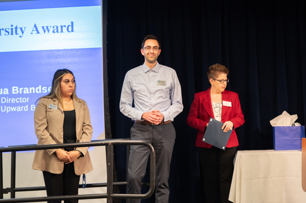 three people on stage during awards ceremony