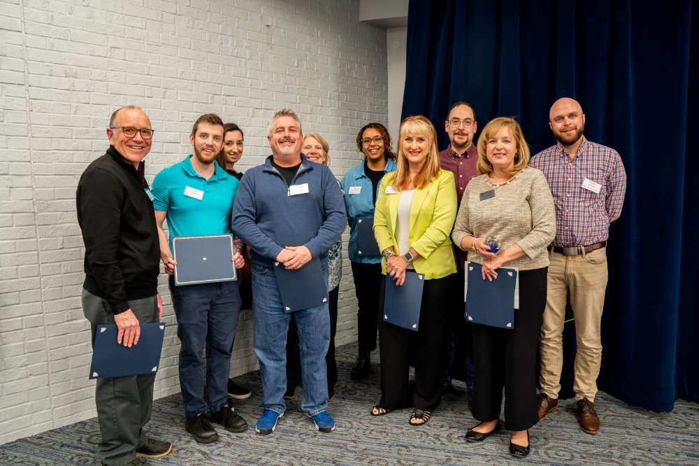 10 people standing and holding certificates after receiving a team award