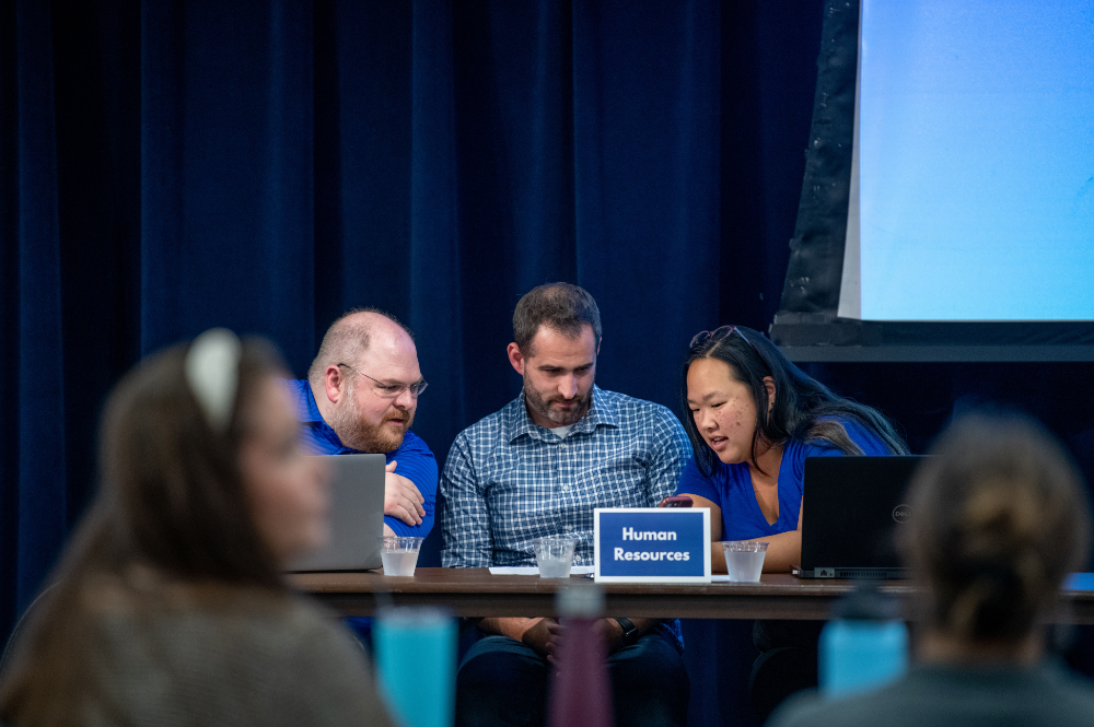Three people seated behind table with Human Resources nameplate in front