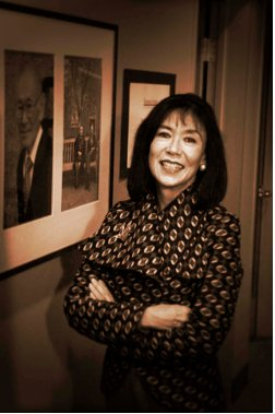 portrait of Karen Korematsu, who stands next to a photograph on the wall of her father