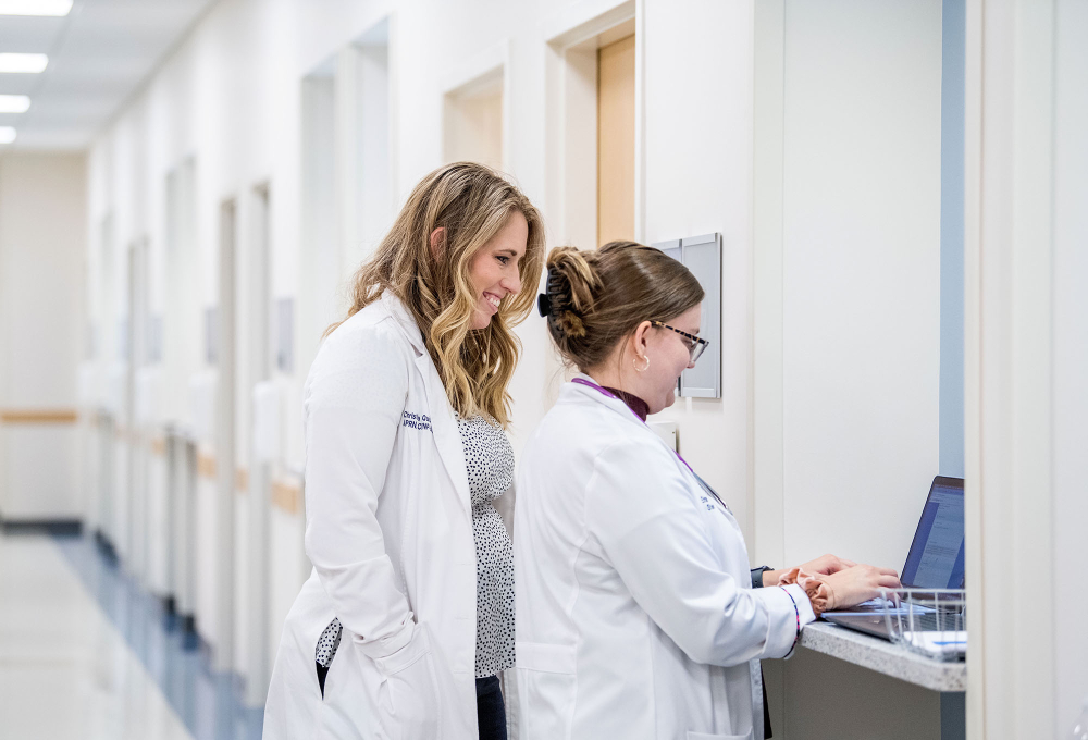 KCON faculty looks over shoulder of nursing student who is typing on laptop, both are standing